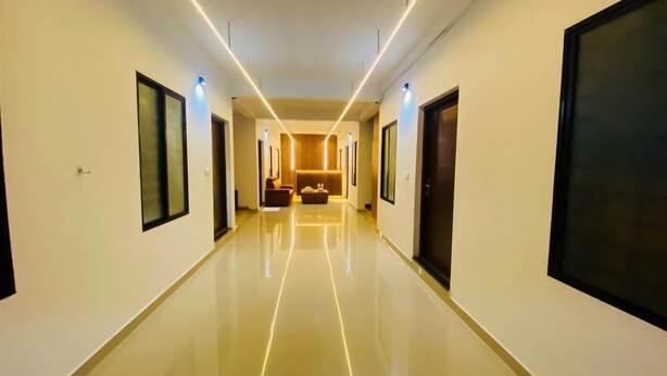 A hotel hallway with a polished floor, framed artwork on the walls, and a seating area in the distance. - Adam Homes (Aluva)
