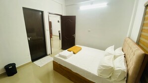 A bedroom with a bed, a door, and a trash bin. - Adam Homes (Aluva)