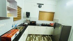 A compact kitchen with white cabinets, a black countertop, a built-in oven, and a window with blinds. - Adam Homes (Aluva)