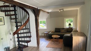 A spacious living room with a wooden staircase, a sofa set, a coffee table, and a view of the outdoors through a window. - Uniquely charming thatched cottage with 900 square meters of land and a view of the Baltic Sea Pure nature (Damp)