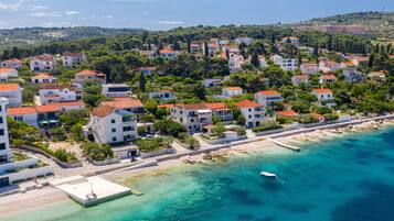 An aerial view of a coastal residential area with buildings, a pier, and clear turquoise waters.