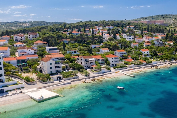 An aerial view of a coastal residential area with buildings, a pier, and clear turquoise waters.
