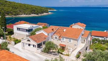 A coastal village with stone houses, a clear blue sea, and a hilly backdrop.