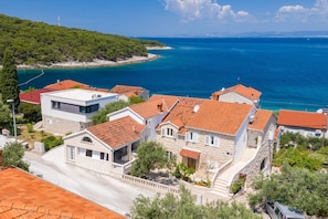 A coastal village with stone houses, a clear blue sea, and a hilly backdrop.
