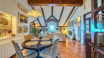 A dining area with a round table, wicker chairs, and a hanging light fixture.