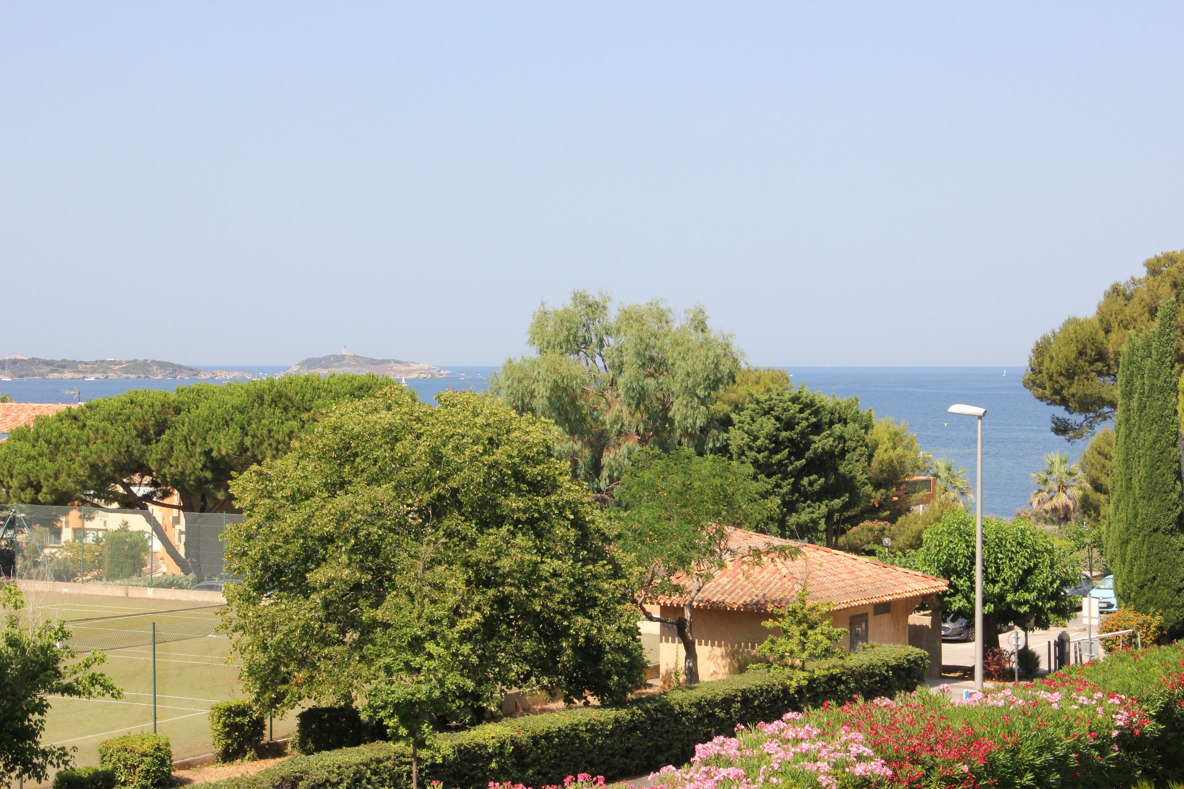 A coastal view with a tennis court, a building with a tiled roof, and a street lamp.