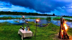 Un área de comedor al aire libre con una mesa lista para dos personas, rodeada por un paisaje natural y una masa de agua.