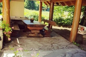A rustic outdoor seating area with a wooden table and benches, surrounded by greenery.