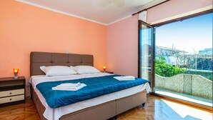 A bedroom with a bed, bedside tables, and a large window with a view of greenery and buildings.