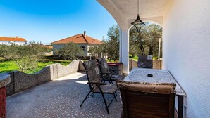 An outdoor patio with a table and chairs, a stone wall, and a view of a house and trees.