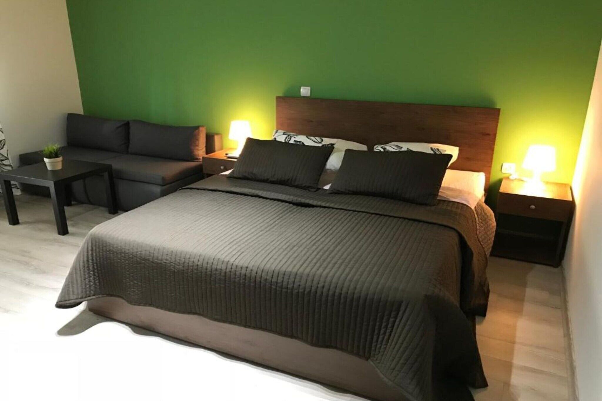 Une chambre d’hôtel avec un grand lit, un canapé, deux tables de chevet avec des lampes et une petite table avec une plante.