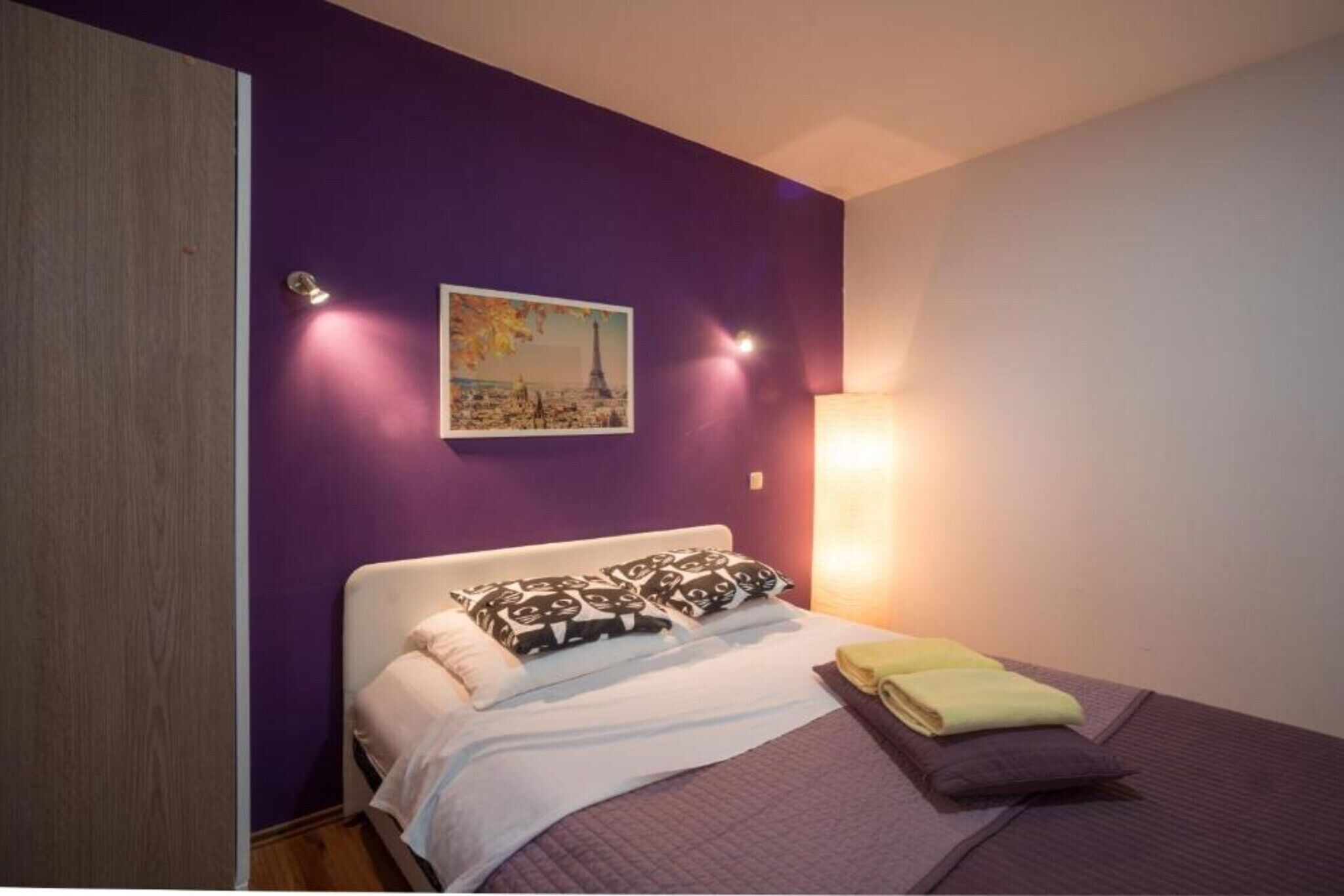 A bedroom with a bed, pillows, a blanket, and a painting on the wall.