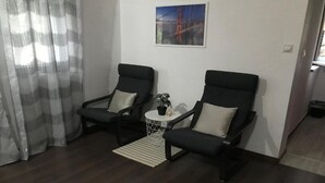 A room with two black chairs, a small white table, a white rug, and a painting of the Golden Gate Bridge.