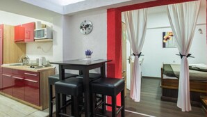 A compact room with a kitchenette, a dining area with stools, a bed with curtains, and a clock on the wall.
