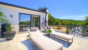 A modern outdoor patio with lounge chairs and a hanging chair, surrounded by potted plants and a scenic view of hills. - Wellness Villa- Four Bedroom Villa with Swimming pool (Grizane)