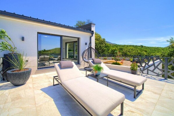 Eine moderne Außenpatio mit Liegestühlen und einer Hängematte, umgeben von Topfpflanzen und einem schönen Hügelblick.