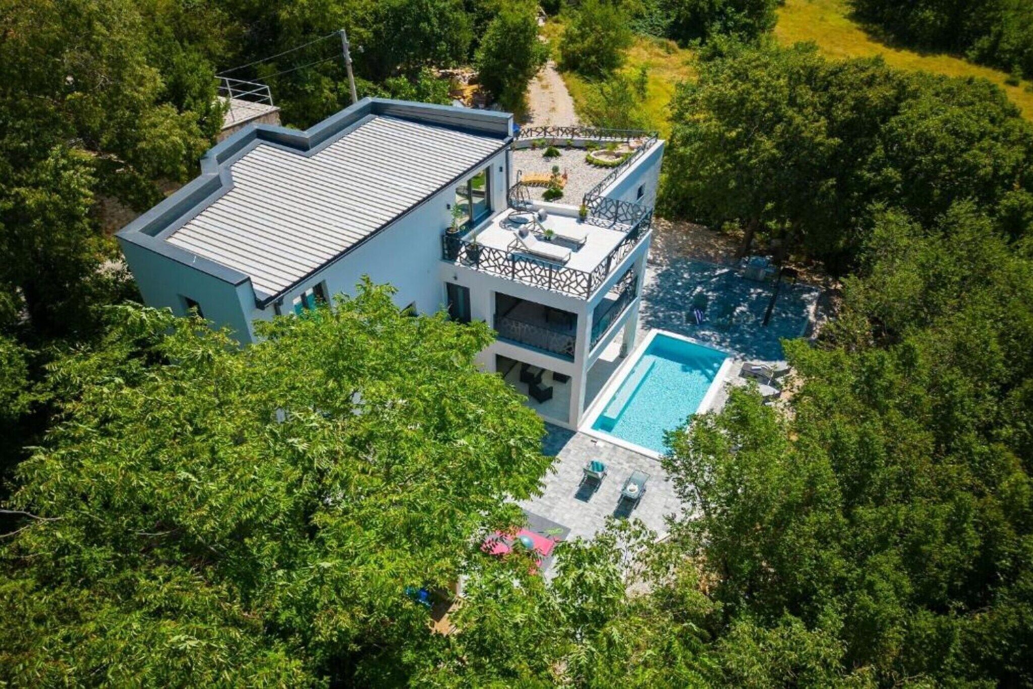 A modern two-story house with a swimming pool, surrounded by lush greenery.
