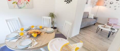 A dining area with a round table set for four, a baby stroller, and a living area with a sofa and a lamp.