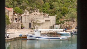 Un barco atracado en un puerto deportivo con un edificio de piedra y vegetación al fondo.