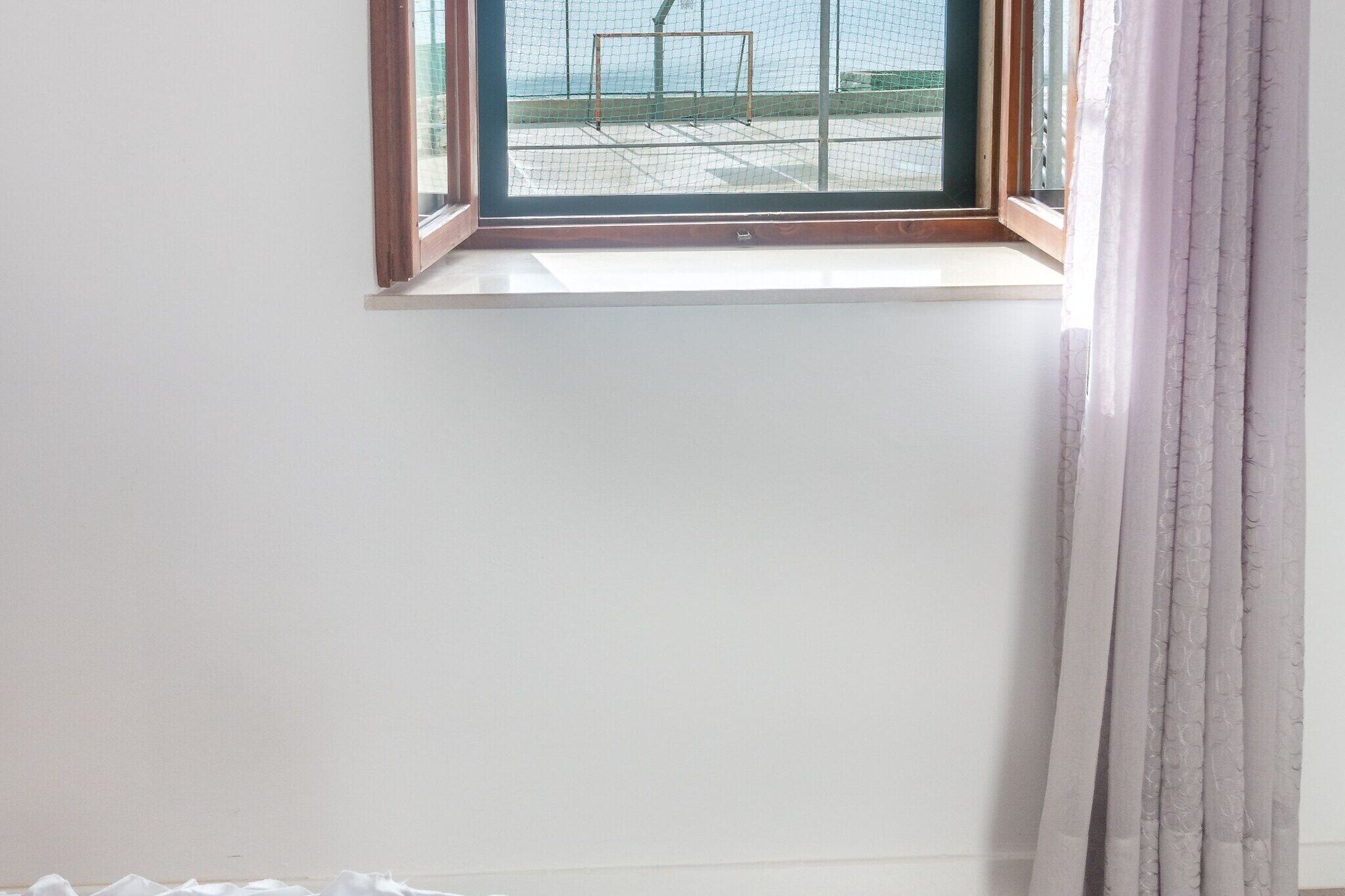 A room with a window, a curtain, and a view of an outdoor area with a metal structure.