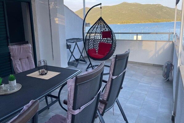 A balcony with a table, chairs, a hanging chair, and a view of the sea.
