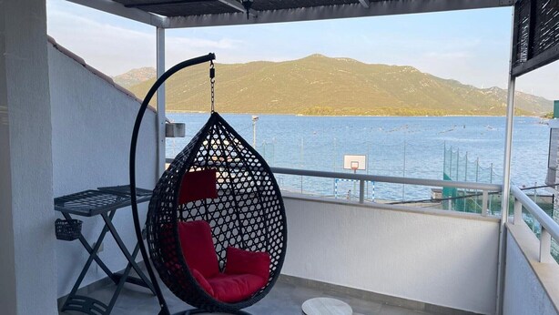 Un balcón con una hamaca colgante, una mesita y vistas al agua y a las montañas.