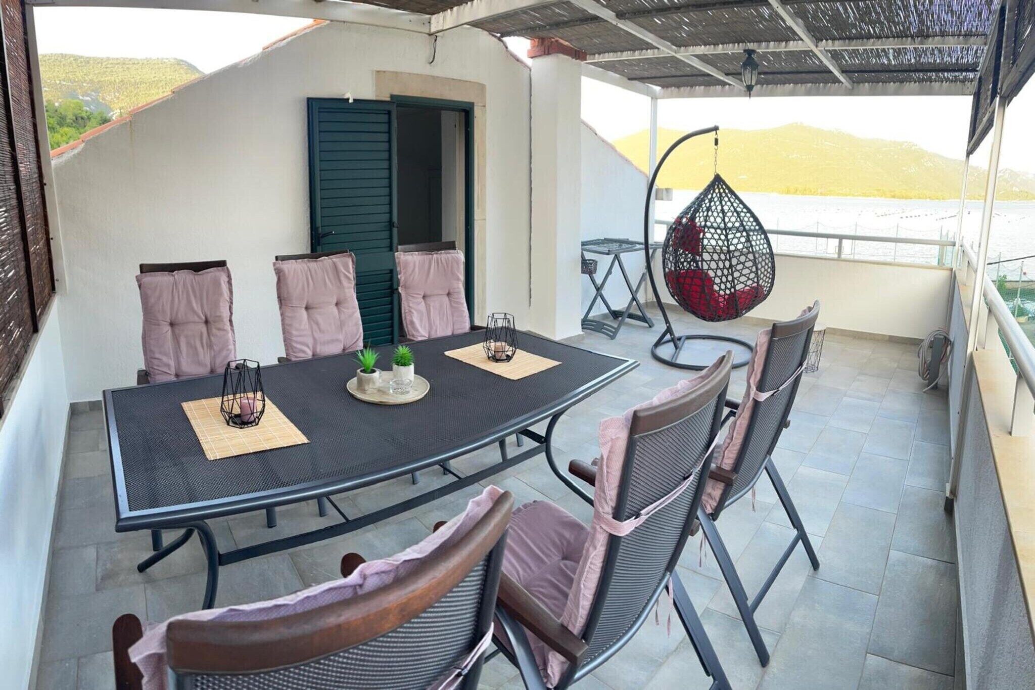 A covered outdoor dining area with a round table, chairs, and a hanging chair.