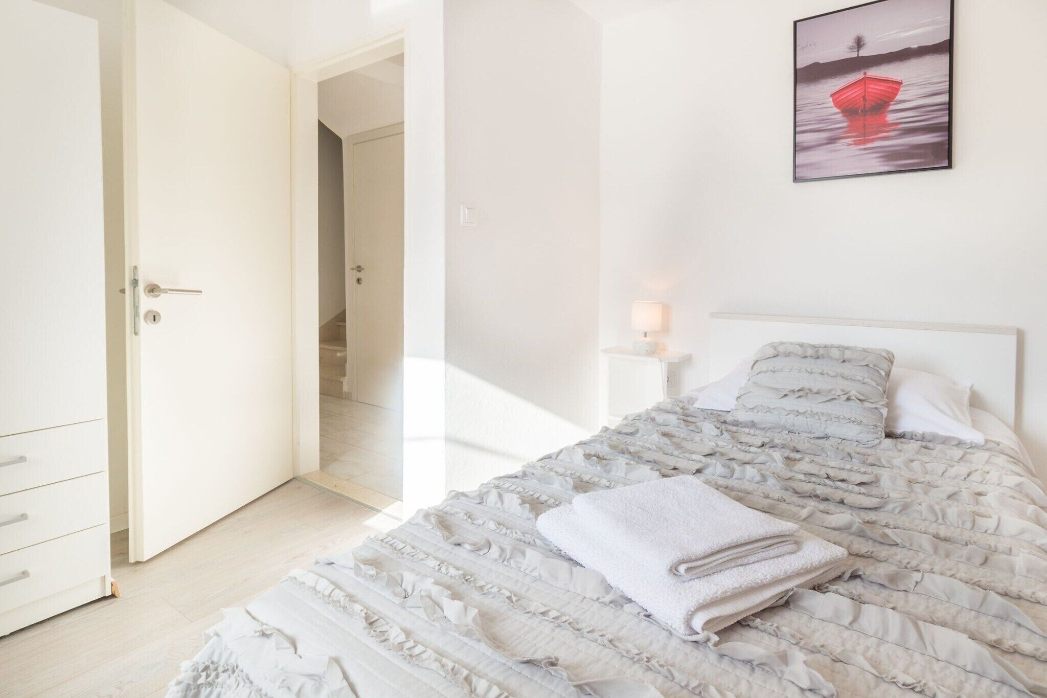 Une chambre à coucher comprenant un lit, une table de chevet, une lampe et une porte donnant sur une autre pièce.