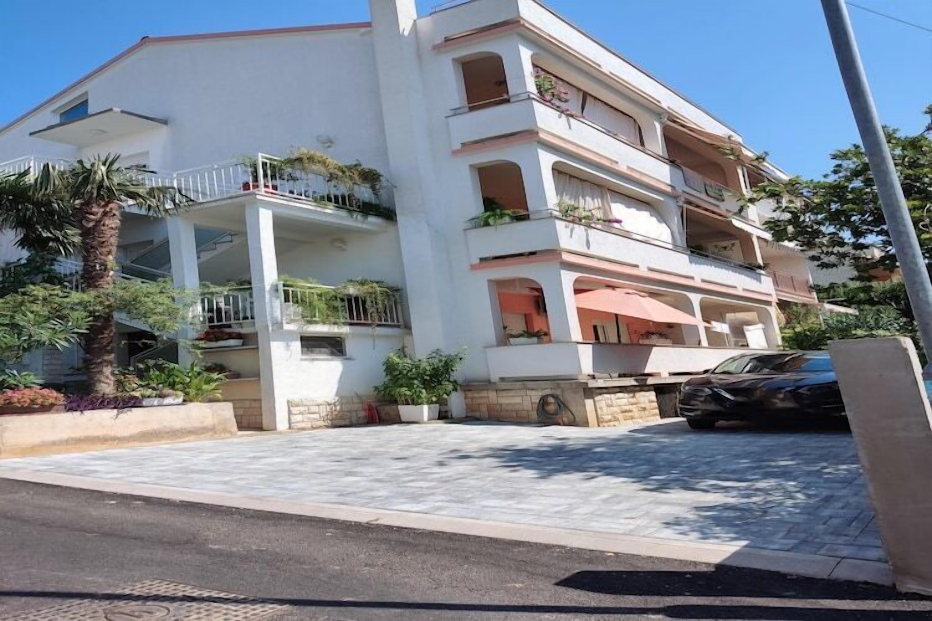 Un edificio de varios pisos con balcones, un camino de entrada pavimentado y un coche estacionado.