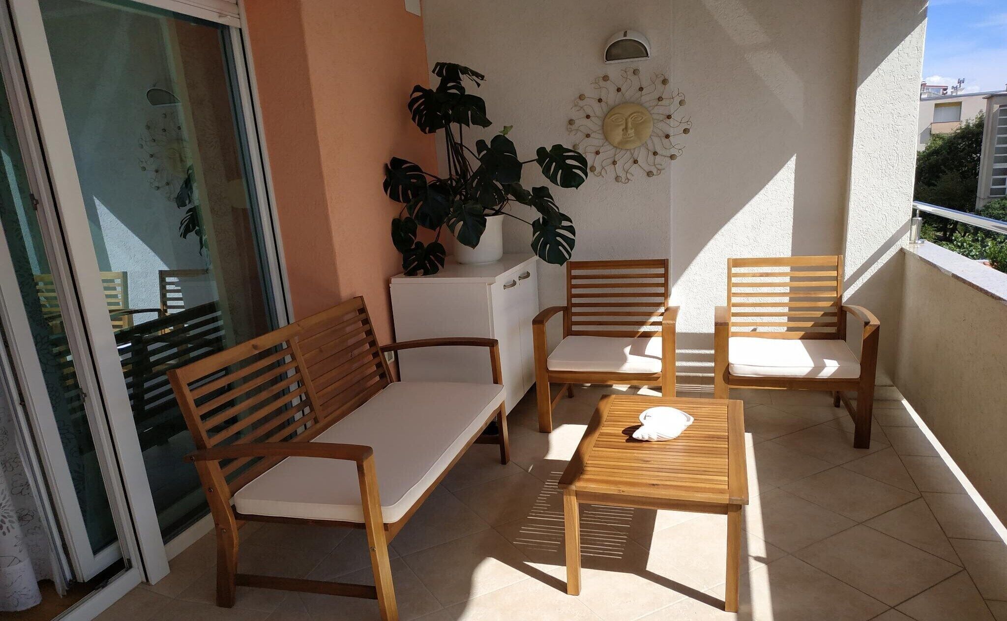 Un balcón con muebles de madera, una planta en maceta y un adorno en la pared.