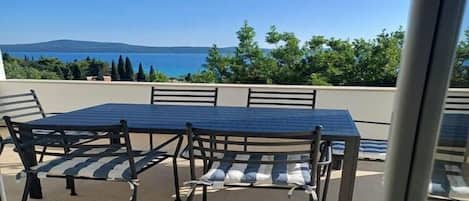 Un espace extérieur aménagé avec une table et des chaises, offrant une vue panoramique sur la mer et les collines.
