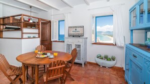 A dining area with a wooden table, chairs, and breakfast items. There is a view of the sea through a window. - Casa Dafne Sperlongaresort (Sperlonga)