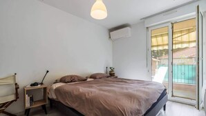 A bedroom with a bed, bedside table, lamp, and a view of a balcony. - Large 2 room apartment and beautiful terrace (Niza)