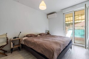 A bedroom with a bed, bedside table, lamp, and a view of a balcony.