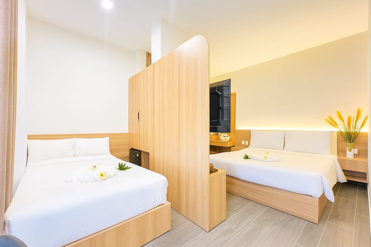 Moderni hotellihuone, jossa on kaksi sänkyä, puinen vaatekaappi, yöpöytä lampun kanssa ja peili.