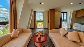 Uma sala de estar moderna com dois sofás bege, uma mesa de centro e vista para um horizonte urbano através de grandes janelas.