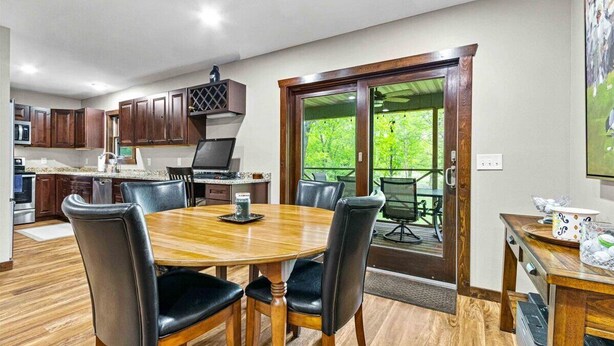 A modern kitchen with dark wooden cabinets, a central island, and a dining area with a wooden table and chairs. - Spacious Lake Arrowhead Golf Course Retreat (Nekoosa)