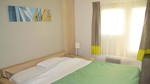 A hotel room with a bed, a window with curtains, a wall-mounted air conditioner, and a painting. - Gite in Normandy Near Sandy Beach (Port-Bail-sur-Mer)