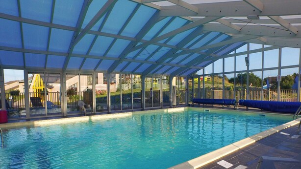 An indoor swimming pool with clear blue water, surrounded by a glass enclosure and a tiled floor. - Gite in Normandy Near Sandy Beach (Port-Bail-sur-Mer)