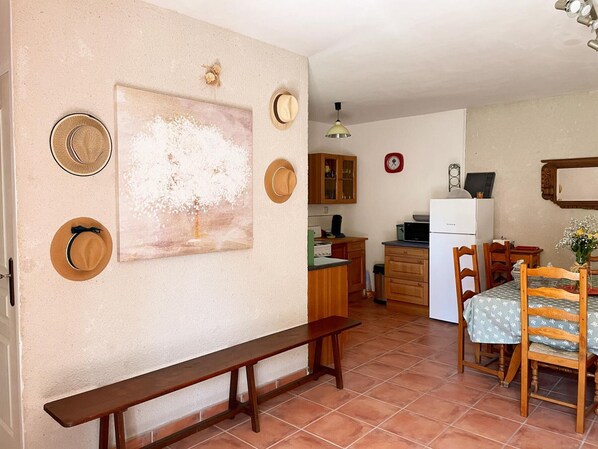 Une cuisine compacte avec un coin repas, comprenant un banc, des placards en bois et une simple horloge murale.