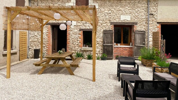 Un espace extérieur aménagé dans un style rustique, avec une pergola en bois, une table de pique-nique et plusieurs fauteuils confortables.
