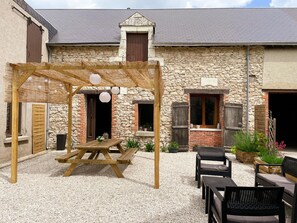 Un espace extérieur aménagé dans un style rustique, avec une pergola en bois, une table de pique-nique et plusieurs fauteuils confortables.