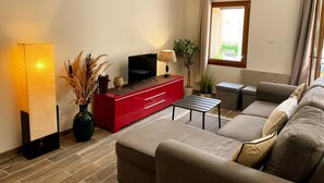 Un salon moderne avec un meuble de rangement rouge pour les appareils multimédias, un grand lampadaire, un canapé et une fenêtre avec des rideaux.
