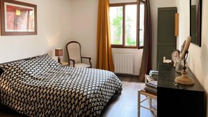 Une chambre à coucher comprenant un lit, une chaise, un bureau avec un miroir, une fenêtre avec des rideaux et un luminaire suspendu.