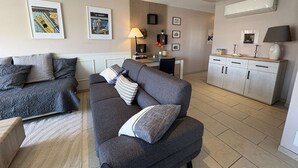 Un soggiorno moderno con un divano grigio, un'area pranzo con tavolo e sedie, e una cucina con mobili bianchi.