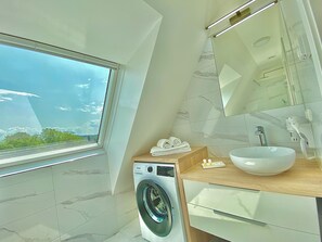 A modern bathroom with a built-in washing machine, a large sink, and a mirror. - Steiner Residences Mödling (Mödling)