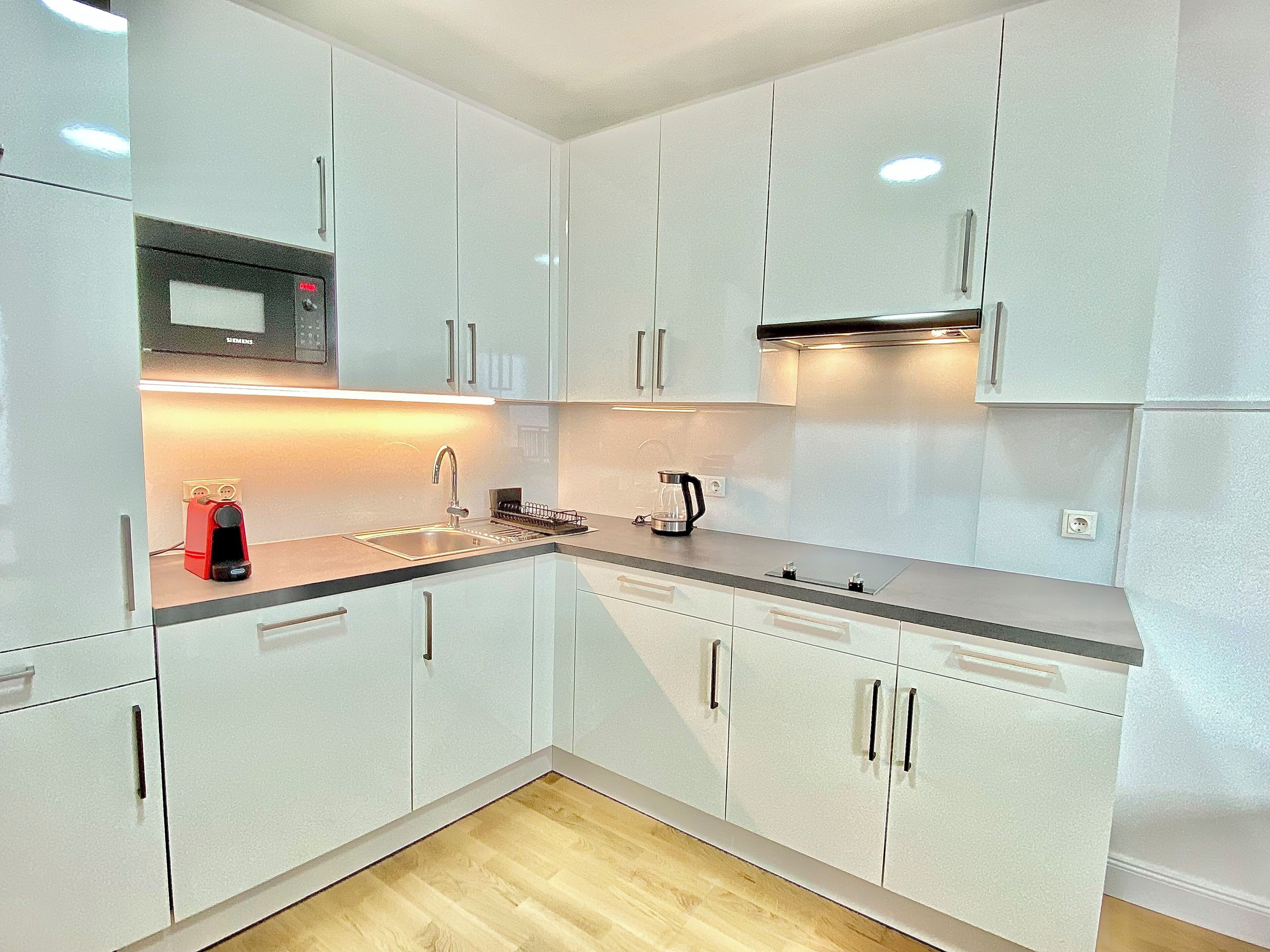 A modern kitchen with white cabinets, a stainless steel sink, a microwave, and a coffee maker.
