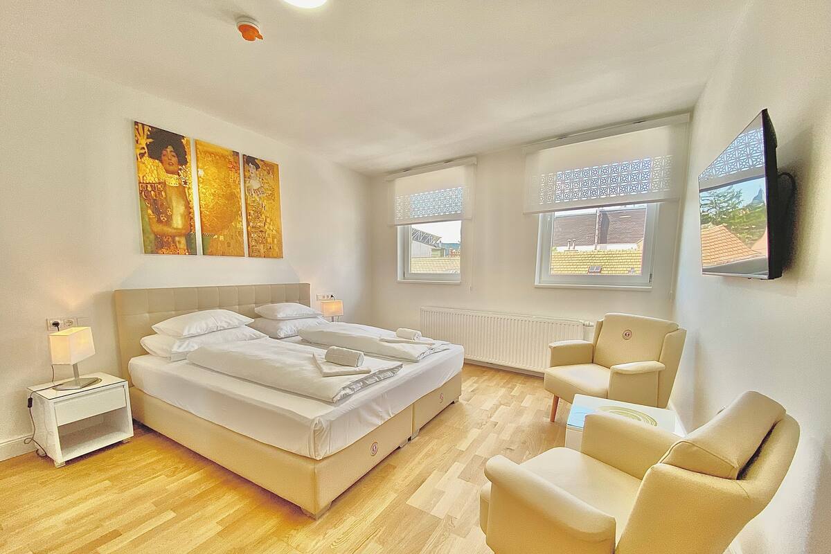 A hotel room with a large bed, two bedside tables, a chair, and a TV on the wall.
