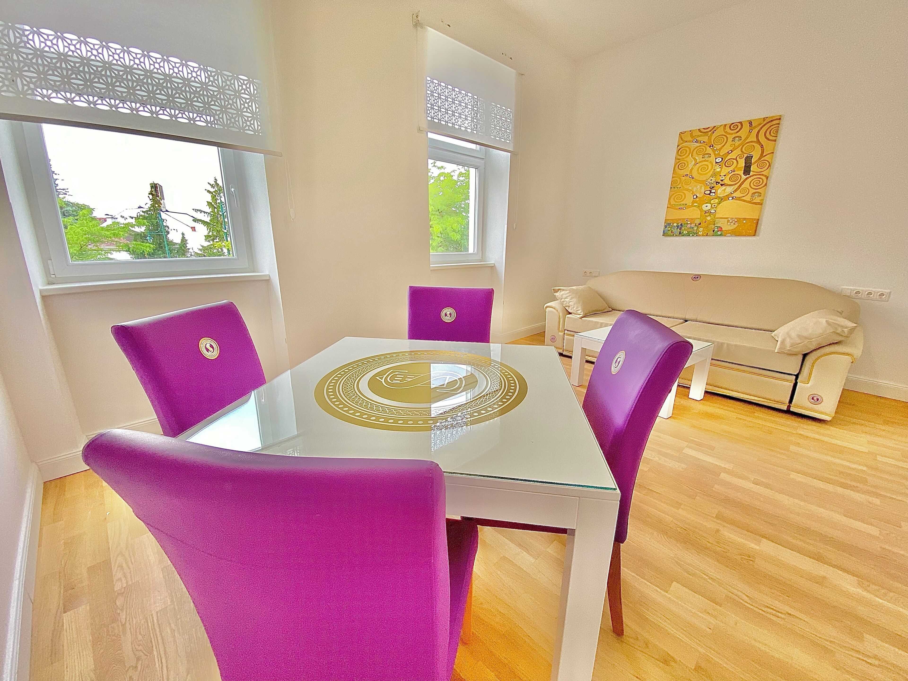 A dining area with a glass table, purple chairs, and a beige sofa.