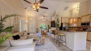 A spacious living area with a sofa, coffee table, and a dining area with chairs. A kitchen with cabinets and appliances is visible in the background. - Poolside Palms Getaway- Near Tampa Brandon Valrico (Valrico)